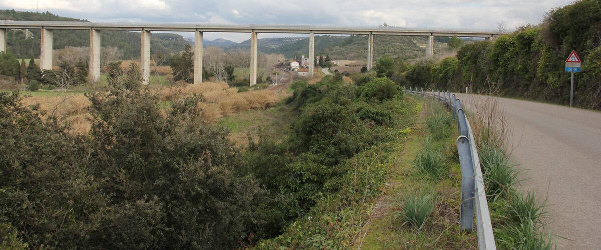 A bridge over a winding road with greenery on either side.