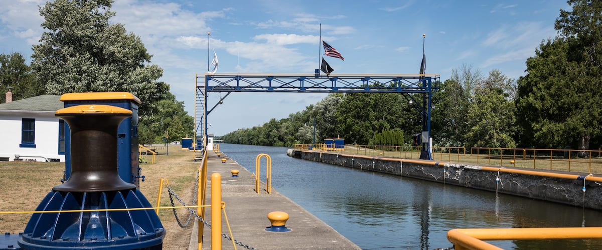 A lock gate with an American flag, a blue and yellow structure, and a river.