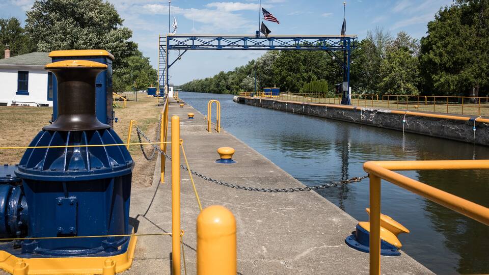 A lock gate with an American flag, a blue and yellow structure, and a river.