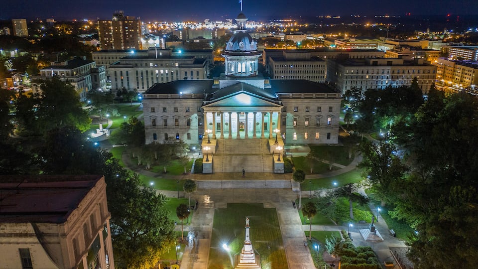 A grand, illuminated building complex with a central dome and a statue in the courtyard.