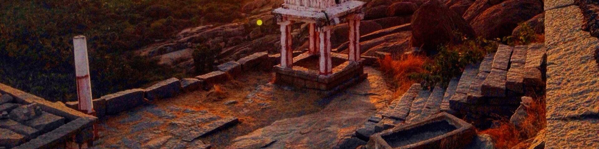 A temple with a white dome and red stripes, surrounded by rocky terrain and a sunset in the background.