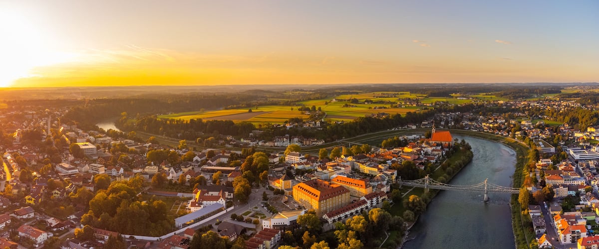 A river flowing through a town with a bridge, surrounded by fields and buildings.