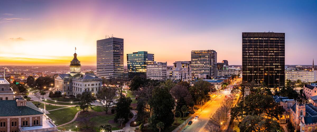 A cityscape at dusk with illuminated buildings, a prominent dome structure, and a well-lit street.