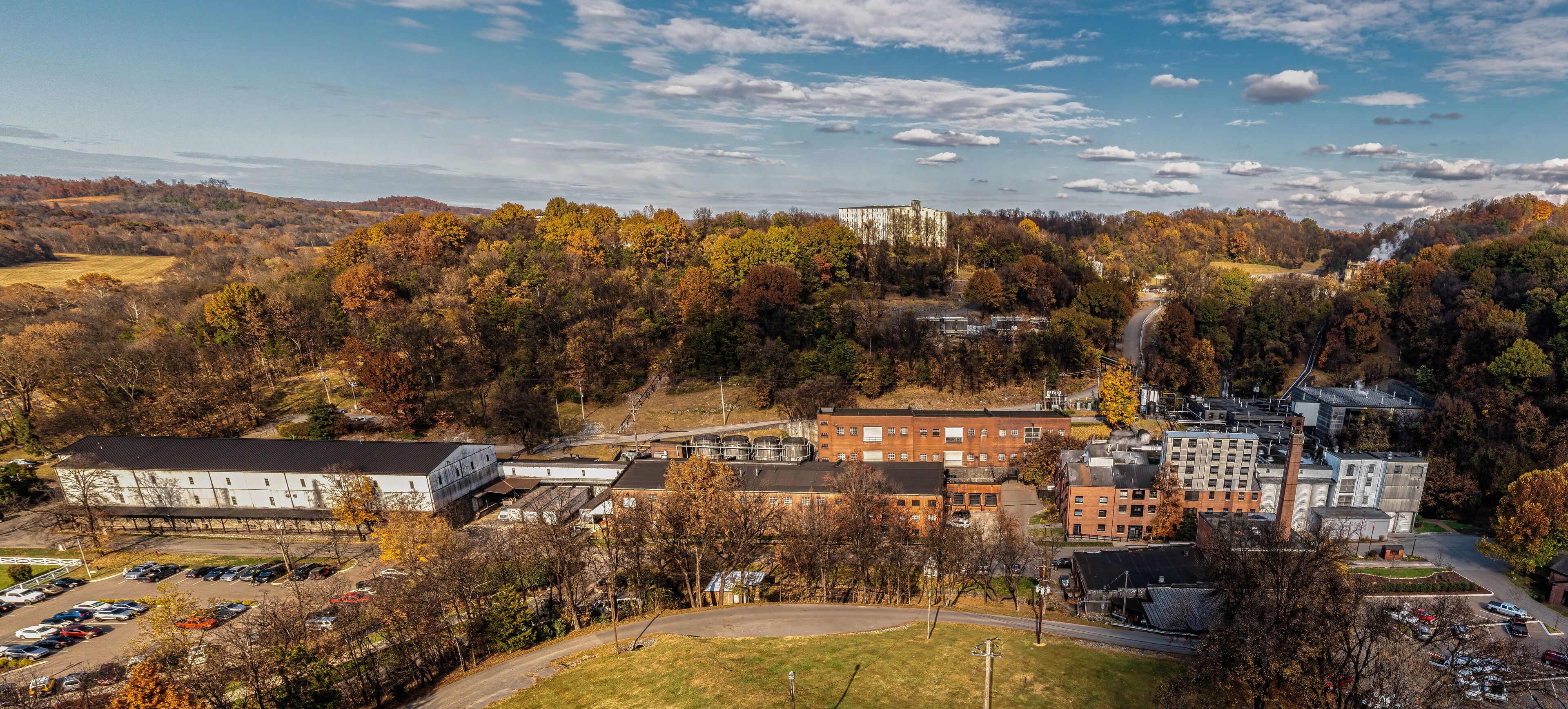 Aerial View of a historic bourbon whiskey distillery and an ageing warehouse on a hill in the background. Autumn colorful fall foliage panorama in Lynchburg Tennessee U.S.A.