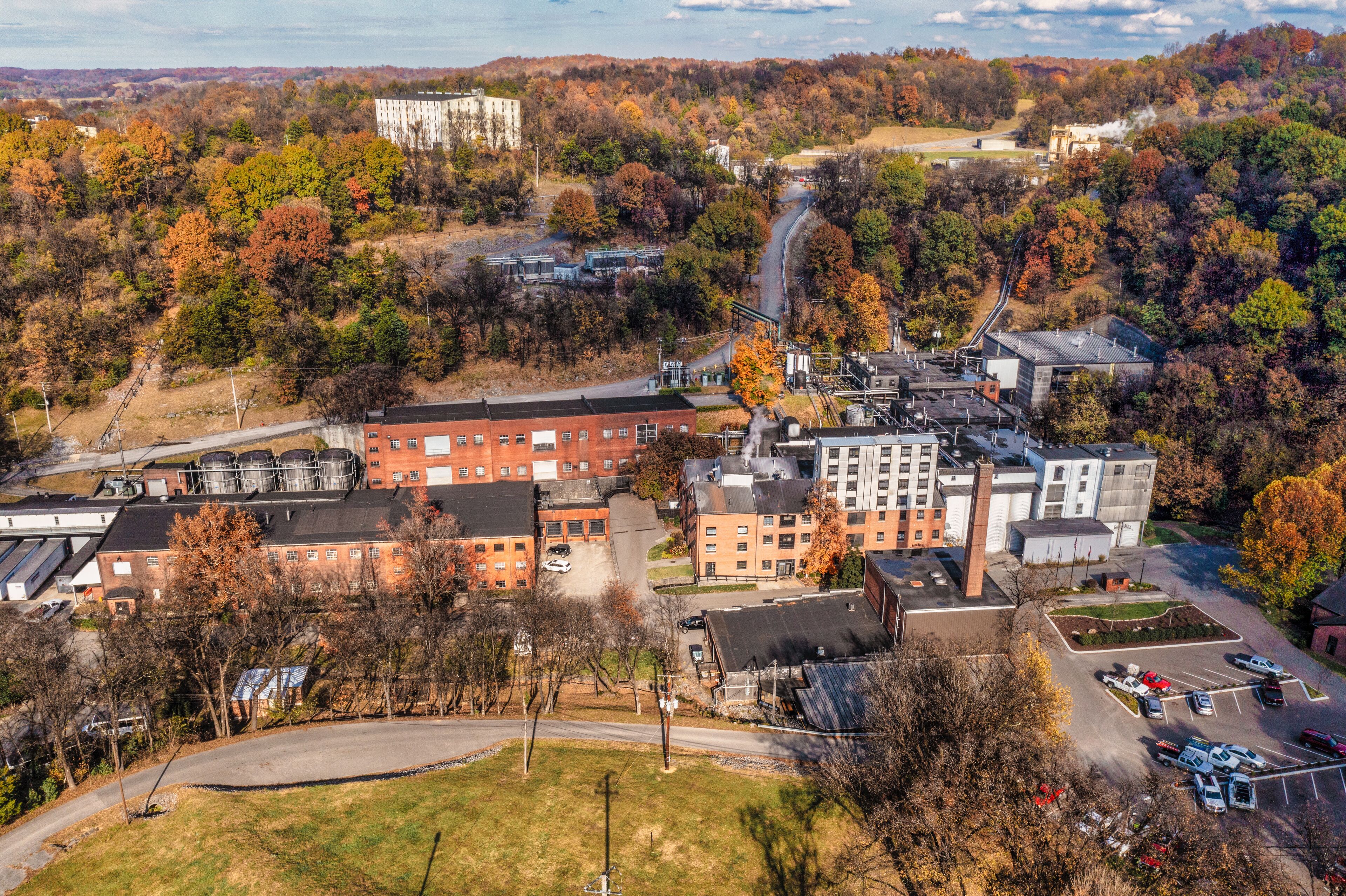 Aerial View of a historic bourbon whiskey distillery and an ageing warehouse on a hill in the background. Autumn colorful fall foliage panorama in Lynchburg Tennessee U.S.A.
