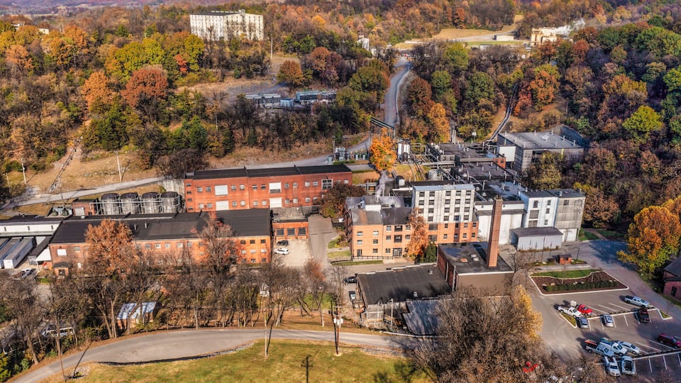 An industrial area with buildings, a parking lot, and autumn-colored trees.