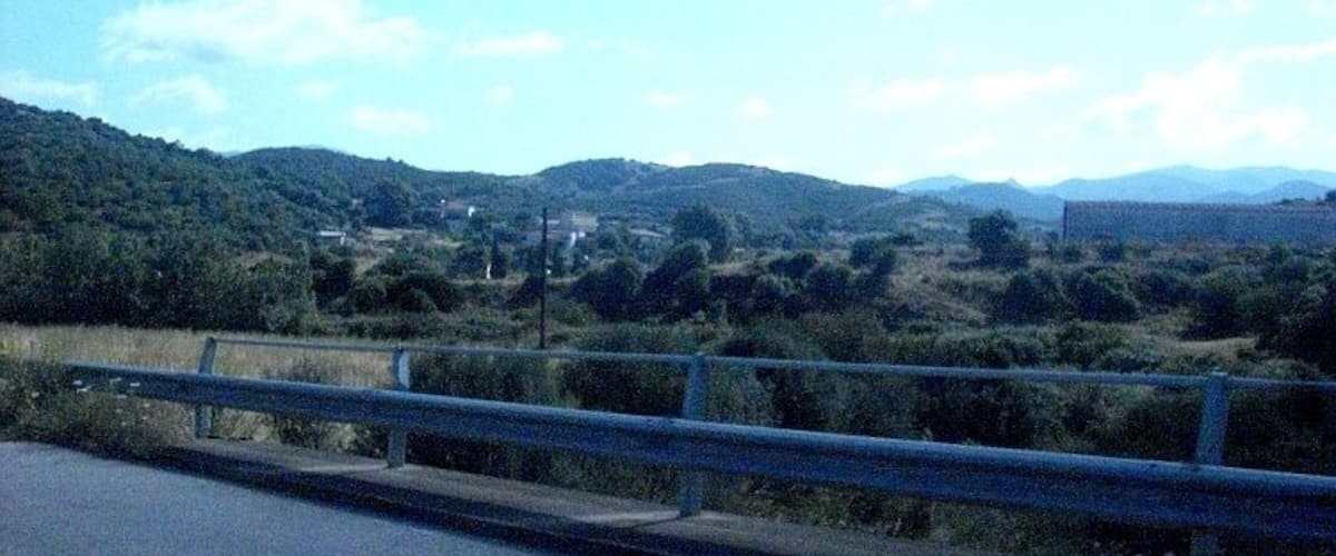 A road with a guardrail, hills, and sparse vegetation.