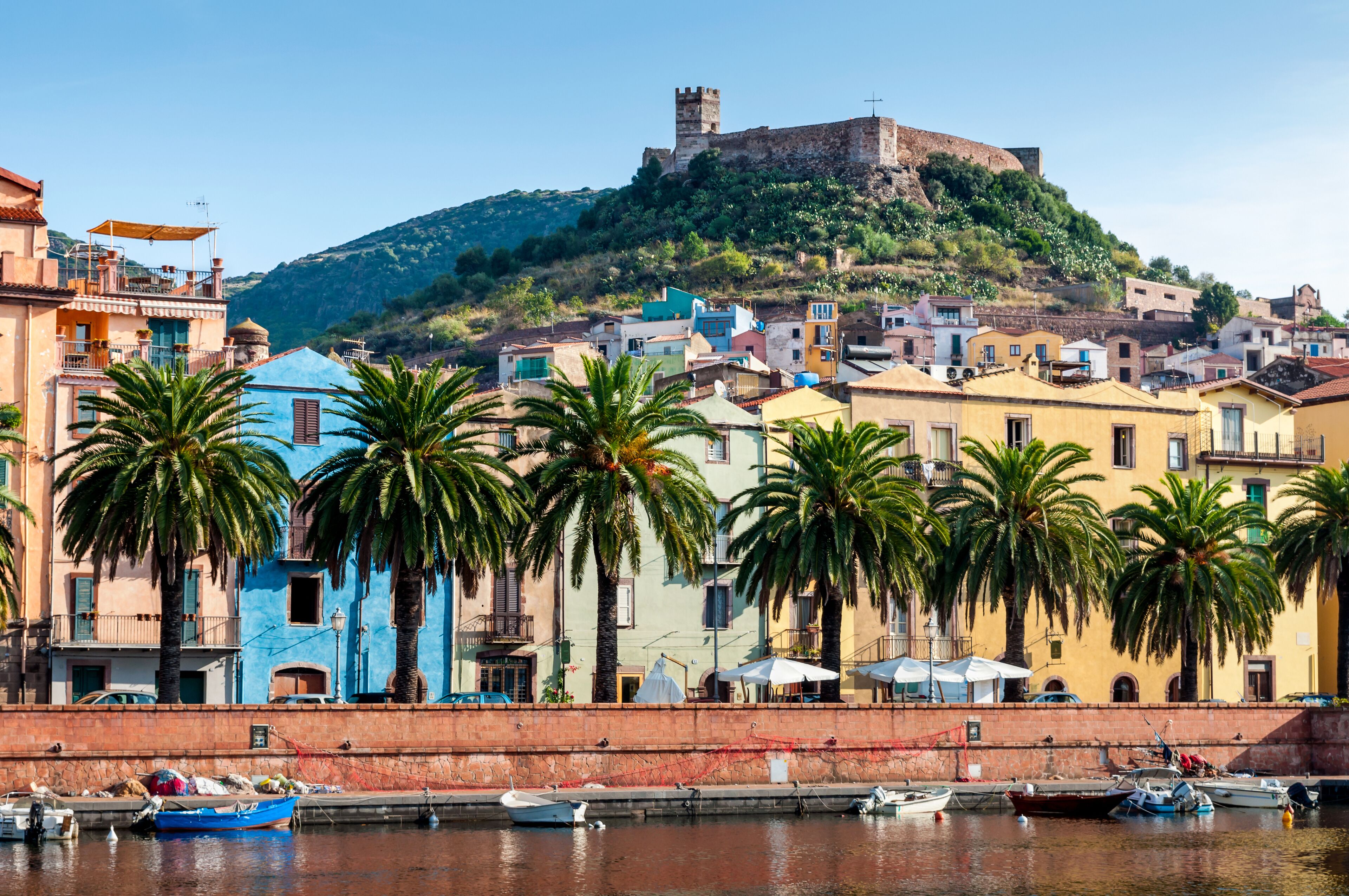 A coastal town with colorful buildings, palm trees, and a historic castle on a hill.