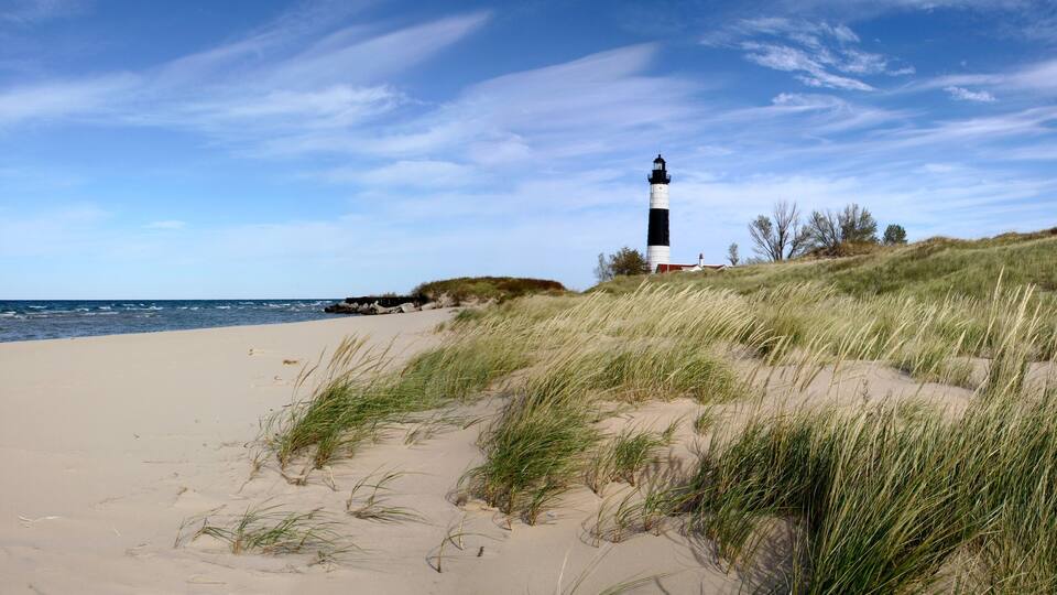 A beach with sand dunes and a lighthouse.