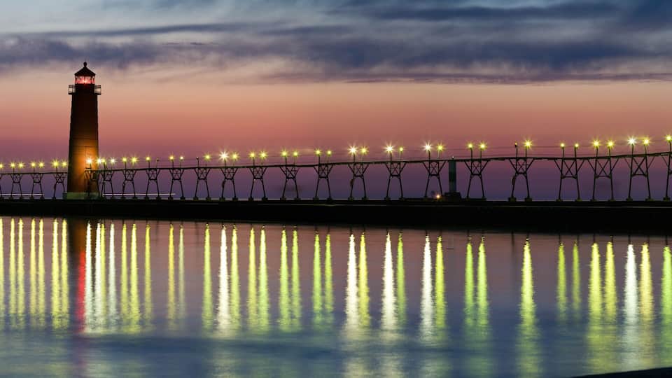 A pier with lights reflecting on the water at dusk.
