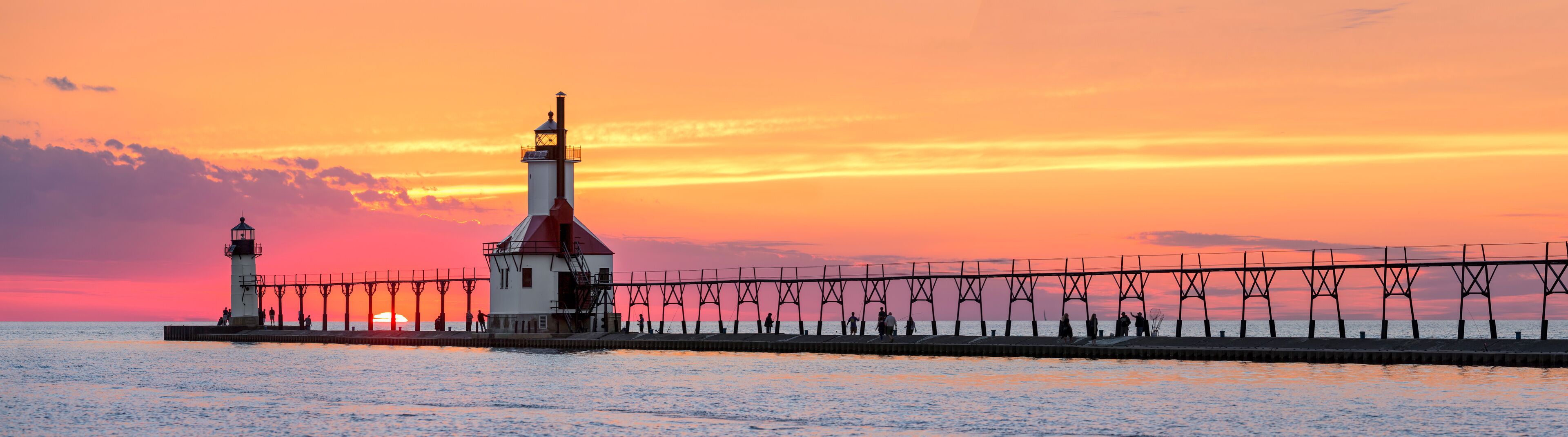 A lighthouse and pier at sunset.