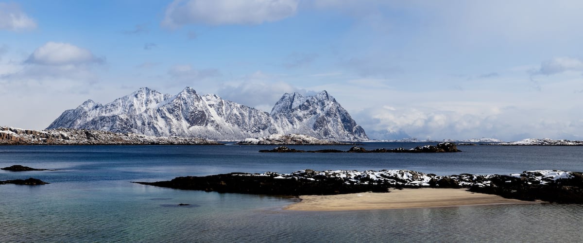 A coastal landscape with snow-covered mountains and a calm sea.