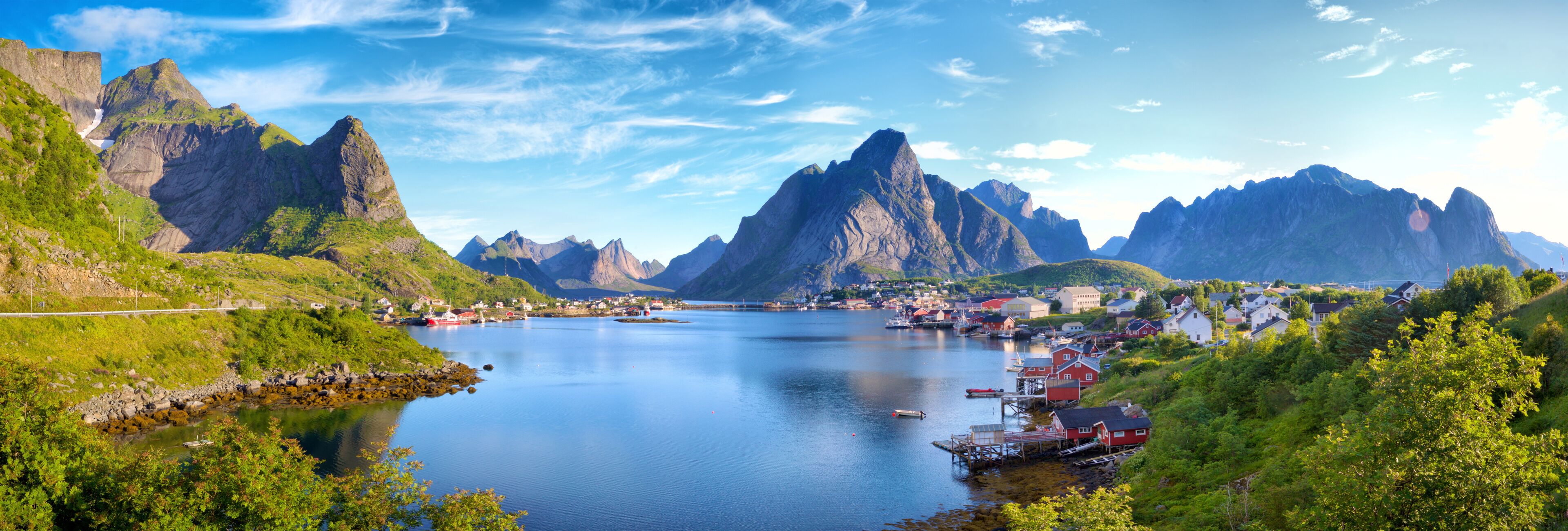 A fjord with steep mountains, a small harbor with boats, and a village with red houses.