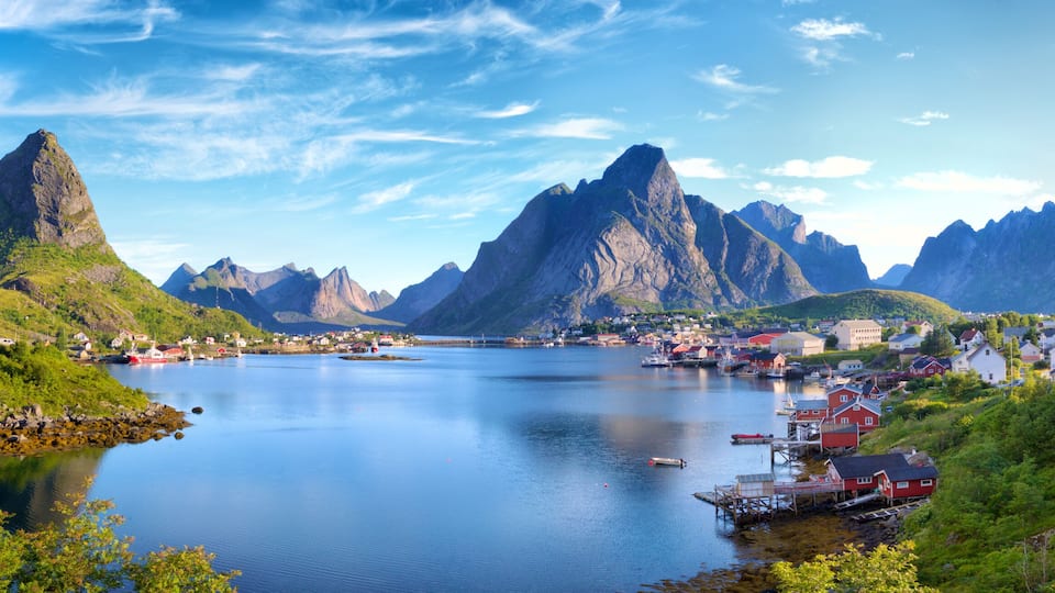 A fjord with steep mountains, a small harbor with boats, and a village with red houses.
