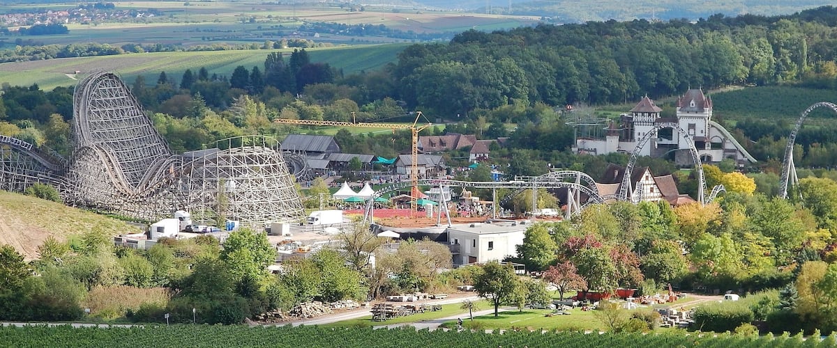Una montaña rusa, un castillo y un paisaje pintoresco con campos y árboles.