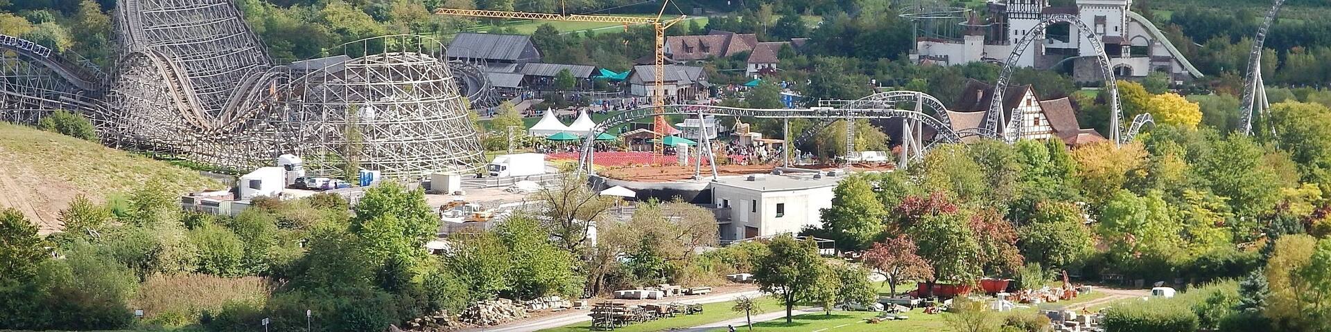 A roller coaster, a castle, and a scenic landscape with fields and trees.