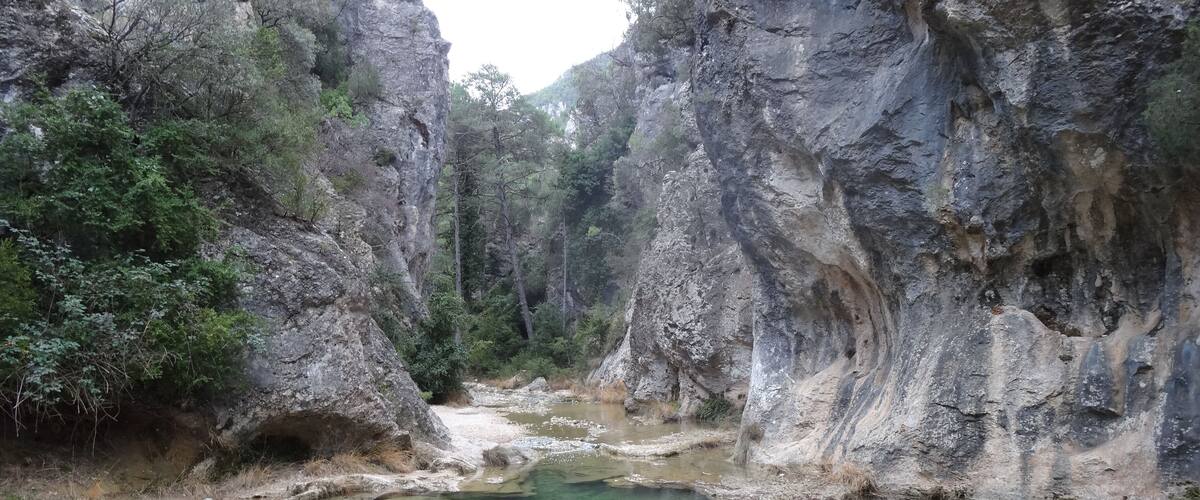 A clear river surrounded by rocky cliffs and dense greenery.