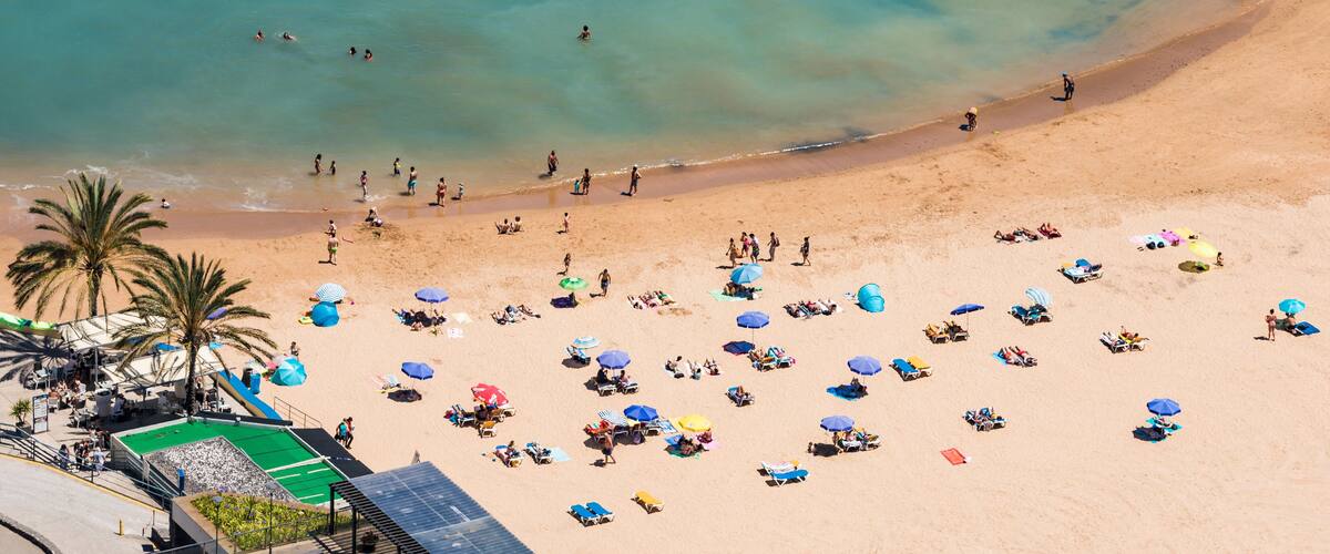 A crowded beach with people swimming and sunbathing under umbrellas.