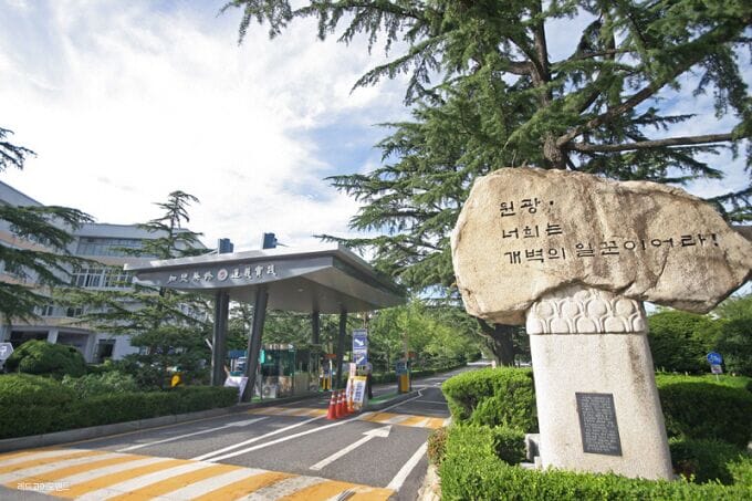 A road sign with Korean text, a covered structure with a sign, and a stone monument with text.