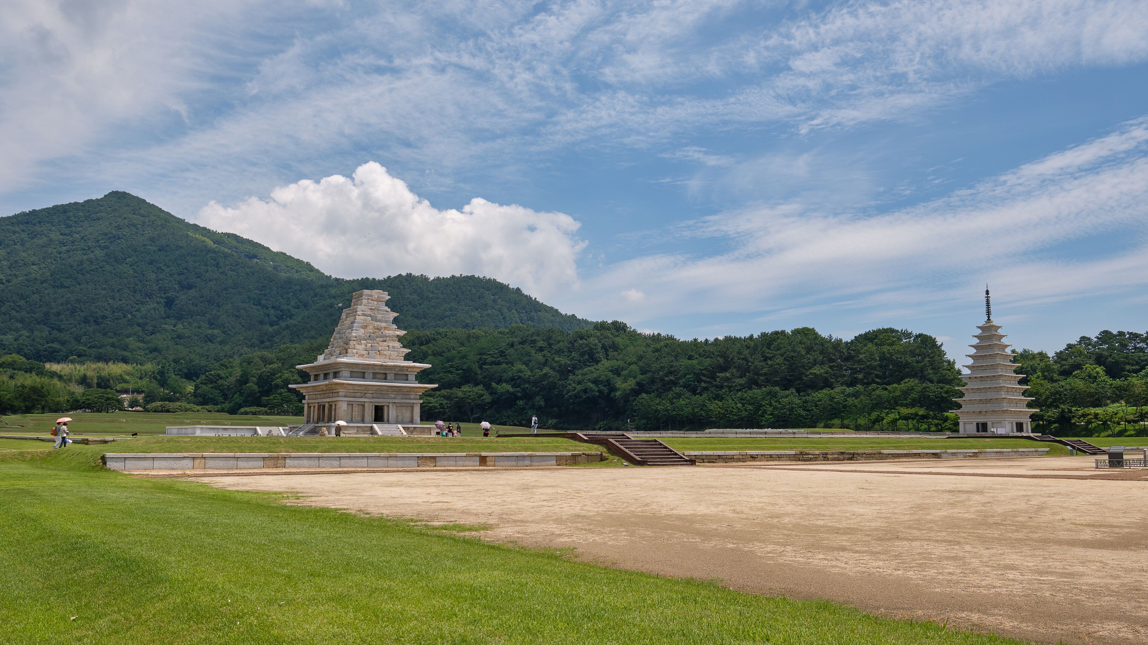 A pagoda and a stupa in a grassy field with a mountain in the background.