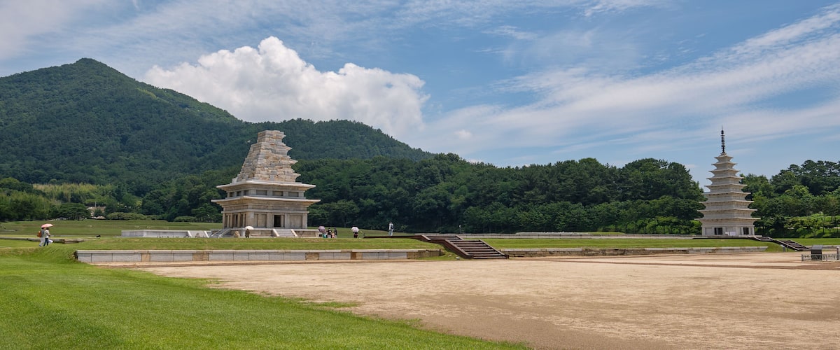 A pagoda and a stupa in a grassy field with a mountain in the background.
