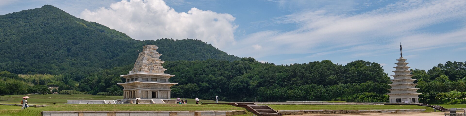 A pagoda and a stupa in a grassy field with a mountain in the background.