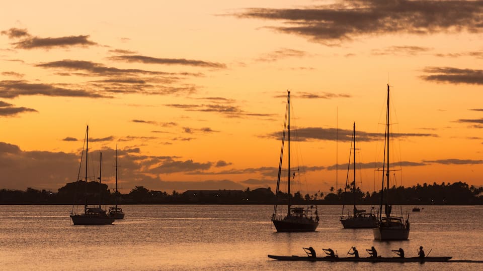 A sunset over a calm sea with sailboats and a rowboat with people.