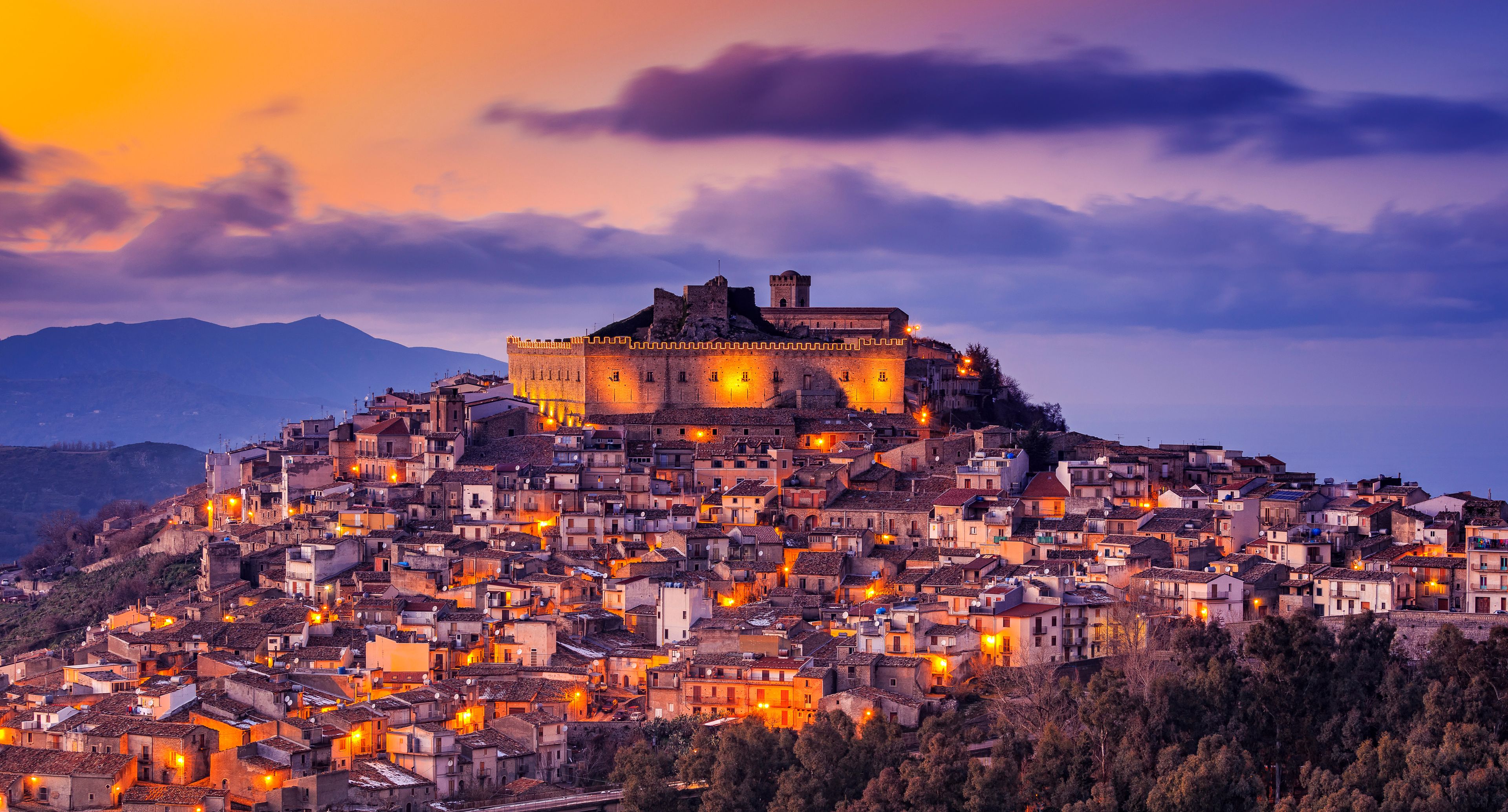 A historic walled town at dusk with a prominent castle on a hill.