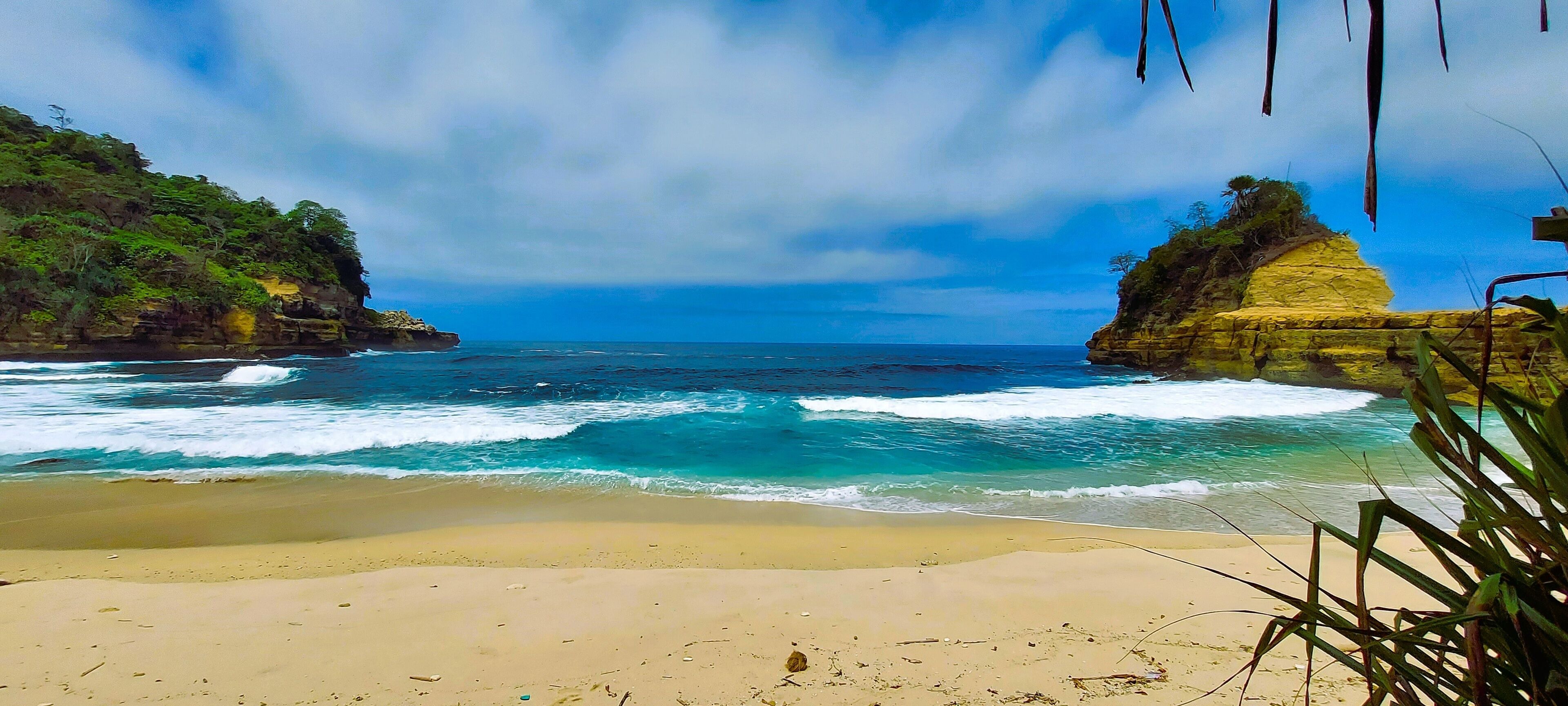 A beach with clear blue waters, sandy shore, and rocky cliffs.