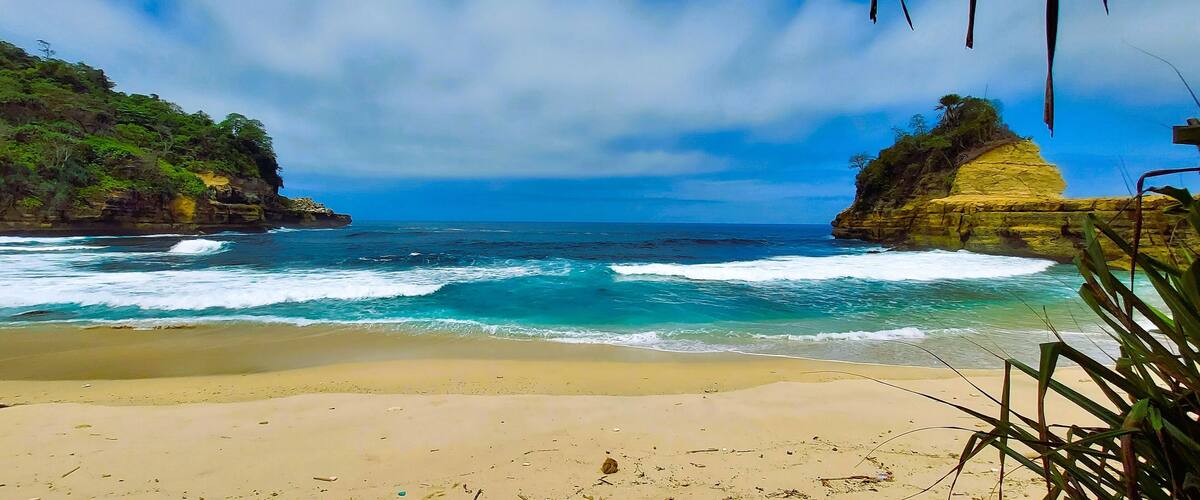 A beach with clear blue waters, sandy shore, and rocky cliffs.