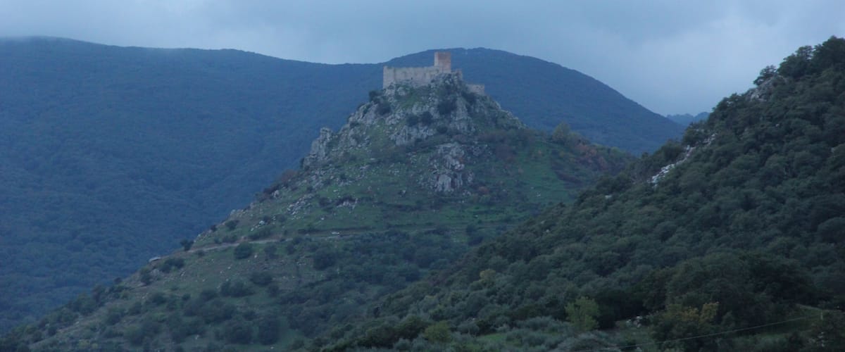 A castle on a hill with surrounding hills and a cloudy sky.