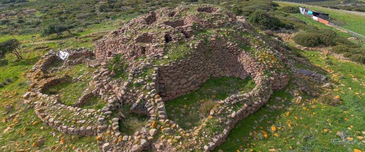A large stone ruin with a circular layout surrounded by green grass and yellow flowers.