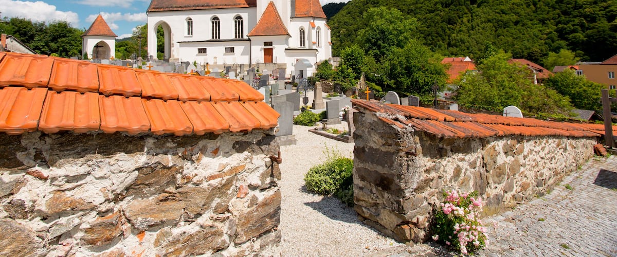 A church with a clock tower, surrounded by stone buildings and a cobblestone path.