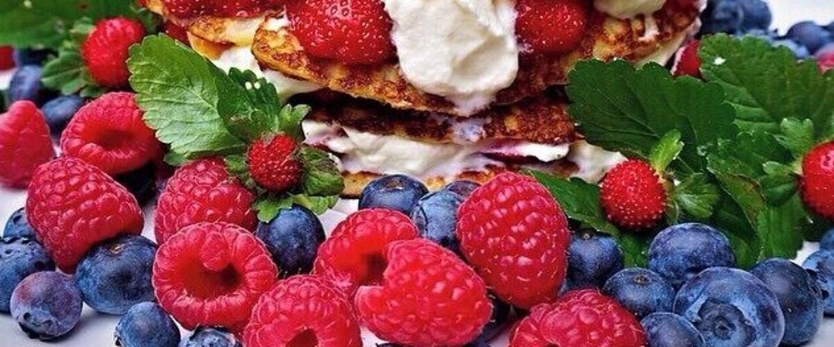 A stack of pancakes with whipped cream and fresh berries.