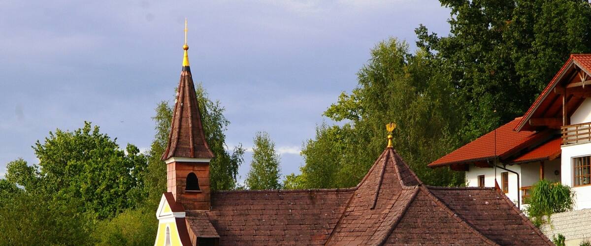 A yellow church with a brown steeple and a bell tower, surrounded by greenery.