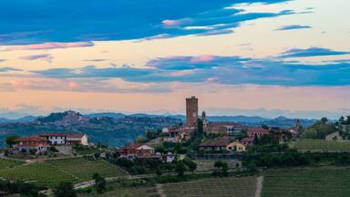 A hillside village with vineyards, a prominent tower, and a mountain range in the background.