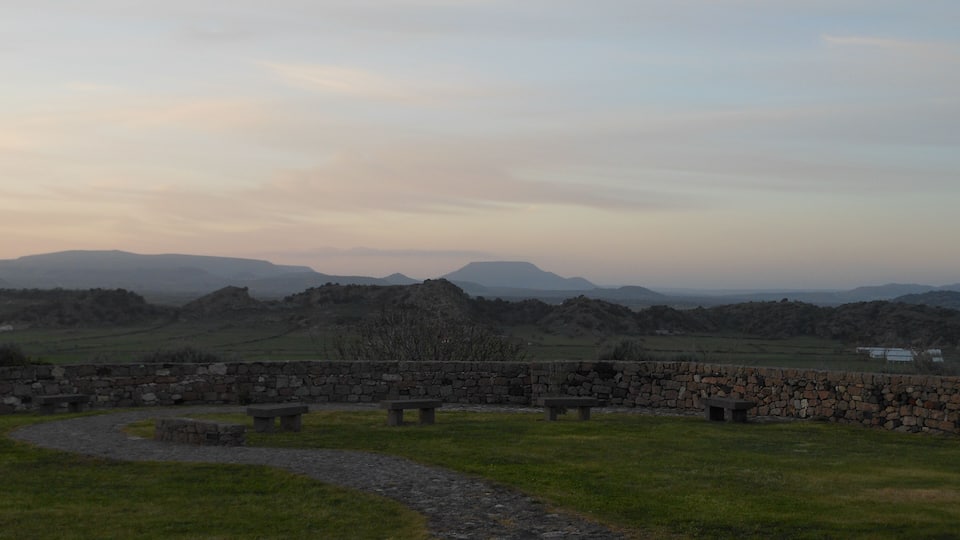 A stone wall with benches overlooking a grassy field and distant hills.