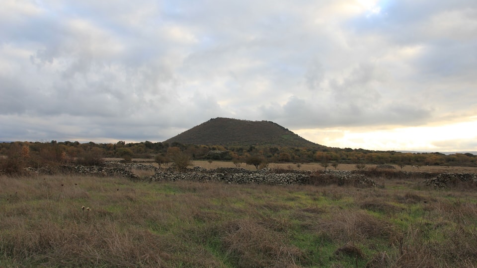 A hill with a stone wall in the foreground and a cloudy sky.