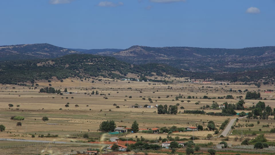 A rural landscape with rolling hills, scattered houses, and fields.