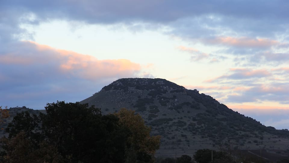 A mountain with sparse vegetation and a cloudy sky.