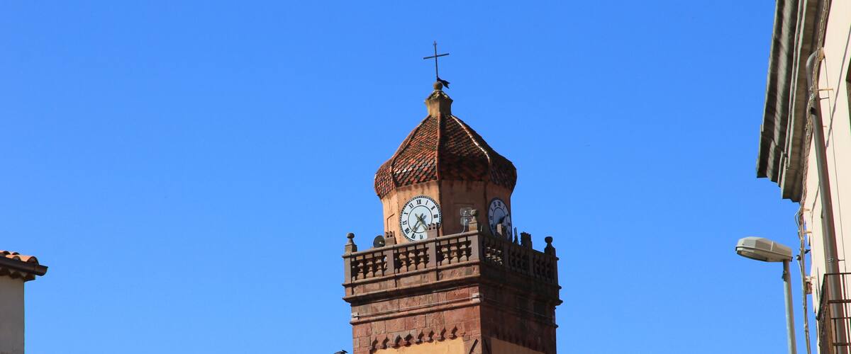 A clock tower with a cross on top, surrounded by buildings.