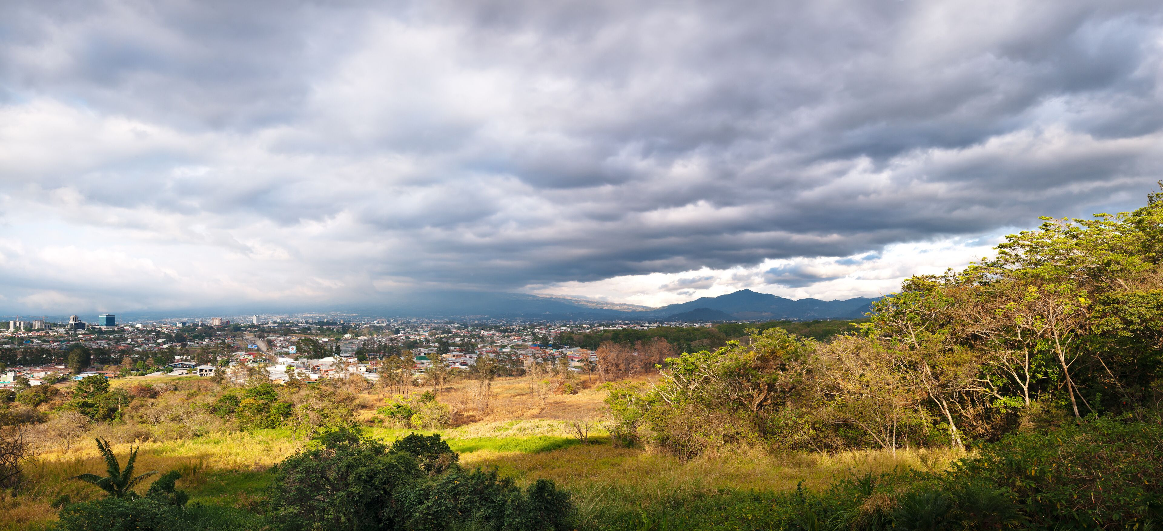 A cityscape with a mountain in the background under a cloudy sky.