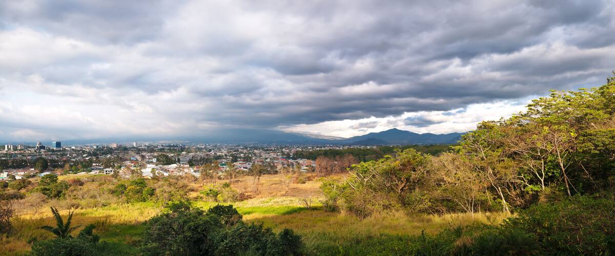 A cityscape with a mountain in the background under a cloudy sky.