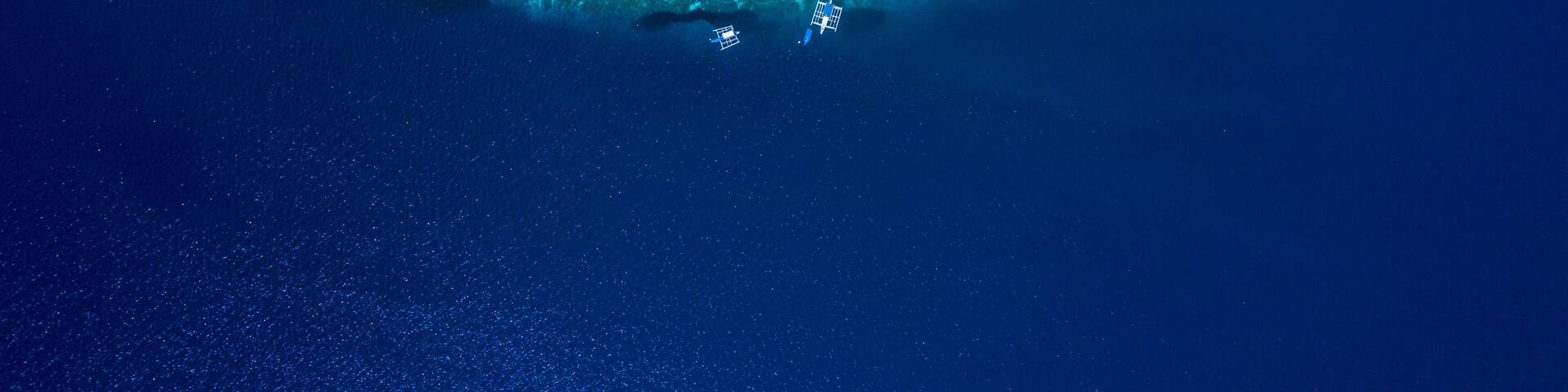 Aerial view of Filipino boats floating on top of clear blue waters, Moalboal is a deep clean blue ocean and has many local Filipino boats in the sea. Moalboal, Cebu, Philippines.