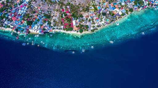 Aerial view of Filipino boats floating on top of clear blue waters, Moalboal is a deep clean blue ocean and has many local Filipino boats in the sea. Moalboal, Cebu, Philippines.