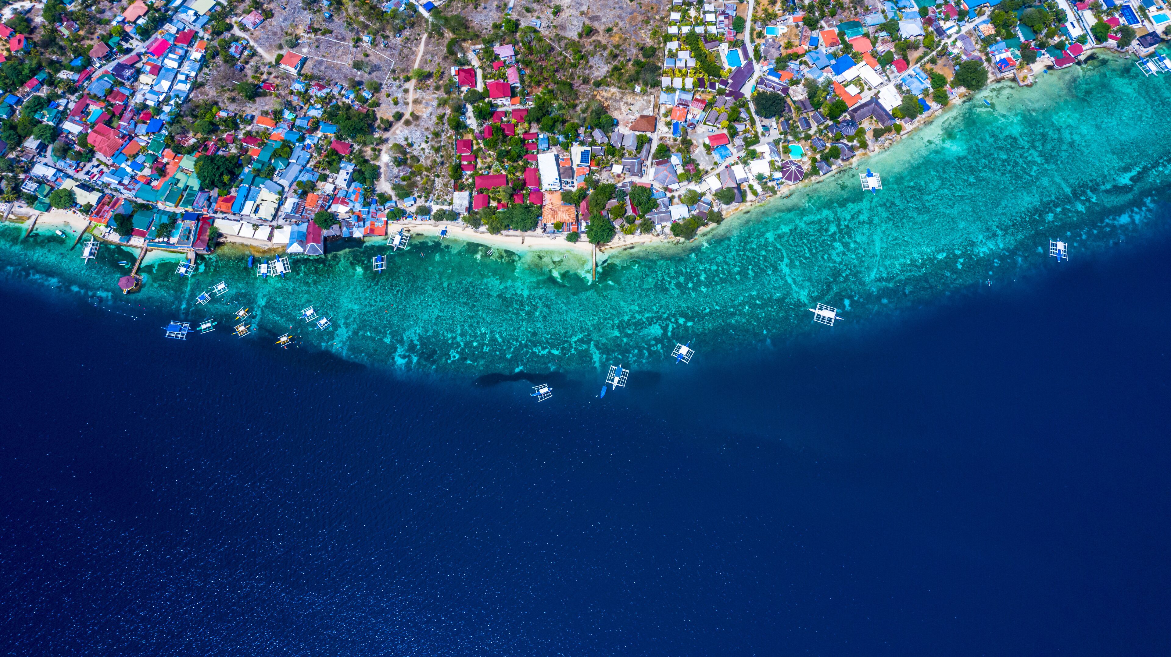 An aerial view of a coastal town with colorful houses, clear turquoise waters, and boats anchored near the shore.