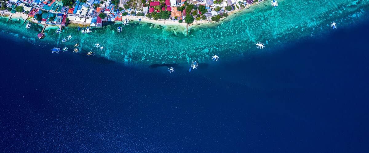 An aerial view of a coastal town with colorful houses, clear turquoise waters, and boats anchored near the shore.