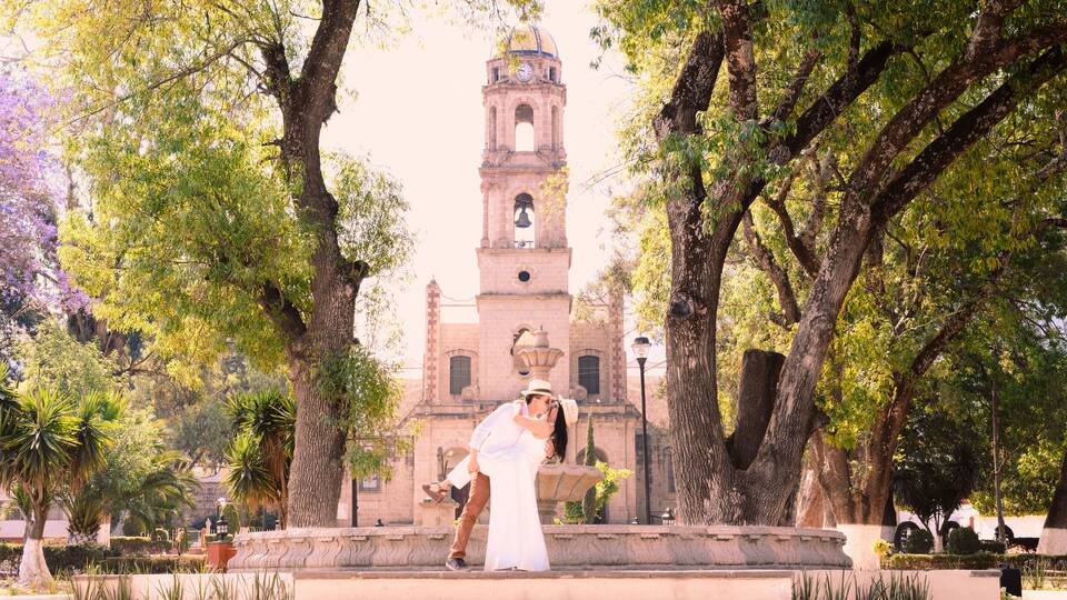 A couple embracing in a park with a historic clock tower in the background.