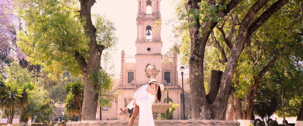 A couple embracing in a park with a historic clock tower in the background.