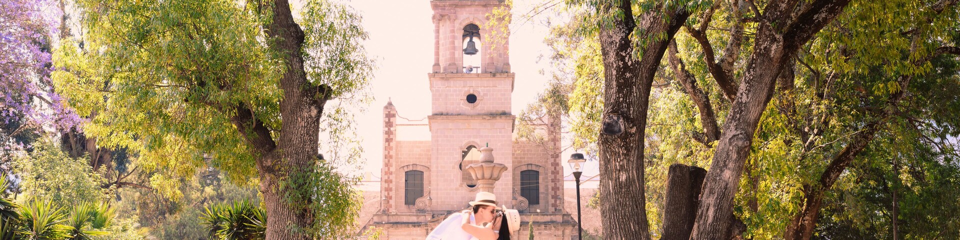 A couple embracing in a park with a historic clock tower in the background.